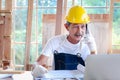 Elderly Asian carpenter with mustache wearing antiknock helmet and cloth gloves, talking on mobile phone with customer, senior Royalty Free Stock Photo