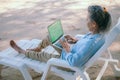 An elderly Asian man happily lounging on his laptop on a relaxing day at the beach Royalty Free Stock Photo