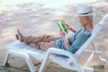 An elderly Asian man happily lounging on his laptop on a relaxing day at the beach