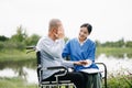 Elderly asian senior man on wheelchair with Asian careful caregiver and encourage patient, walking in garden. with care from a Royalty Free Stock Photo