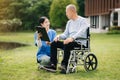 Elderly asian senior man on wheelchair with Asian careful caregiver and encourage patient, walking in garden. with care from a Royalty Free Stock Photo