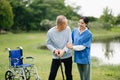 Elderly asian senior man on wheelchair with Asian careful caregiver and encourage patient, walking in garden. with care from a Royalty Free Stock Photo