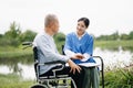 Elderly asian senior man on wheelchair with Asian careful caregiver. Nursing home hospital garden concept