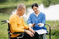 Elderly asian senior man on wheelchair with Asian careful caregiver. Nursing home hospital garden concept