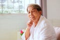 Elderly Asian woman with grey hair sits with her chin on the sofa with a happy smile on her face Royalty Free Stock Photo