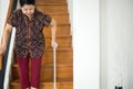 Elderly Asian woman holding sticks while walking down stair at home