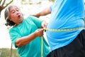 An elderly Asian woman measures the waist circumference of an elderly man with a tape measure. Royalty Free Stock Photo