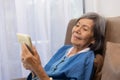 Elderly asian woman relax on couch in living room browsing wireless Internet on tablet Royalty Free Stock Photo