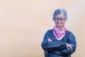 An elderly Asian woman with short gray hair wearing a black leather jacket and colorful scarf, standing and arms crossed on light Royalty Free Stock Photo