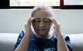 Elderly Asian woman sitting and having a headache and touching her head with her hands at home Royalty Free Stock Photo