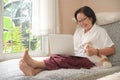 Elderly asian woman sitting on a sofa is using a laptop. She smiled happily, chihuahua dog sat on the side Royalty Free Stock Photo