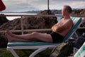 An elderly bald man with glasses lies on a sun lounger and sunbathes on the seashore in Antalya Turkey among the rocks Royalty Free Stock Photo