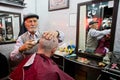 Elderly barber cuts and shaves the client in small hair saloon