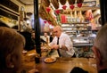 Elderly barman is serving ready-made meals for drinking visitors of tapas bar with vintage decor