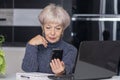 An elderly, beautiful woman holding a smartphone in her hand, sitting in front of her laptop. Concept: communication via the Inter