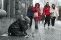 Elderly beggar woman on her knees asking for food from brightly dressed passers-by on the street Royalty Free Stock Photo