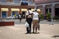 Elderly black-skinned couple walking through a park in an ancient city, with bags in their hands