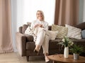 elderly blond woman sit on couch at home holding knitting needles and yarn knits clothes for loved ones