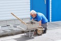 Elderly builder mason tile foundation of house. Working tiler at work outside on summer day.