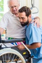 Elderly care nurse helping senior from bed to wheel chair Royalty Free Stock Photo