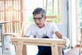 Elderly carpenter wearing safety glasses, working at wooden desk with different craft tools, enjoying his DIY hobby, senior crafts