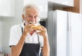 An elderly Caucasian man wearing an apron Eating homemade sandwich bread Royalty Free Stock Photo