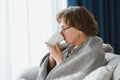 elderly caucasian pensioner wrapped in gray plaid and drinking hot tea in living room Royalty Free Stock Photo