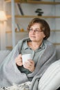 elderly caucasian pensioner wrapped in gray plaid and drinking hot tea in living room Royalty Free Stock Photo