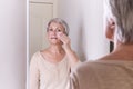 A elderly Caucasian women with short gray hair in casual clothes cares for the skin of the face.