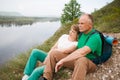 Elderly couple with backpacks sits on the mountain.