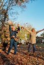 Elderly couple happily throws autumn fall leaves sitting in a park. Positive emotions of the elderly