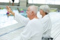 Elderly couple lying waving at someone on pool deck Royalty Free Stock Photo