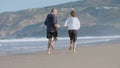 Elderly couple running barefoot on sandy beach and having fun