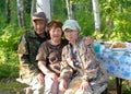 An elderly couple of rural Asian Yakuts and a young girl family pose on a bench at a table in the open air forest in the Northern