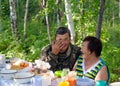 An elderly couple of rural Yakut Asians laugh at a table in an open-air forest in the Northern taiga