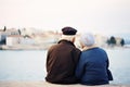 Elderly couple seated side by side on a brick wall, looking off into the distance, AI-generated.