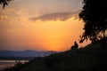 An elderly couple sits on chairs by the lake and looks at the orange sunset.