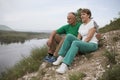 Elderly couple with backpacks sits on the mountain.