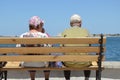 An elderly couple is sitting on a bench by the sea and admiring the seascape, the view from the back