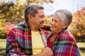 Elderly couple sitting on bench smiling at each other with a blanket Royalty Free Stock Photo