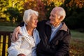 Elderly couple sitting on bench smiling at each other in park Royalty Free Stock Photo