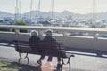 An elderly couple is sitting on a bench among white expensive yachts and mountains on a sunny day. Royalty Free Stock Photo