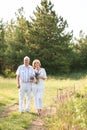 Elderly couple in the white linen dress standing outdoors, in the hands a bouquet of flowers, and on the background of Royalty Free Stock Photo