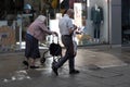 Elderly couple with wife bent over walker and her husband somewhat casually walk past a children\'s shop