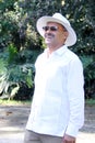 Elderly dark-skinned Latino man in his 60s relaxed in his retirement dressed in a guayabera, hat and sunglasses walks in the park