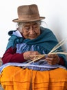 An elderly ecuadorian woman weaves a straw basket