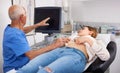 Elderly man sonographer using ultrasonography machine checking female patient in hospital diagnostic room