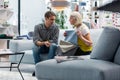 Elderly elegant missis selecting couch textile with adult attractive son