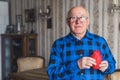 Elderly European bald senior man in blue flannel shirt holding artificial fake heart prop in front of his chest. Old Royalty Free Stock Photo