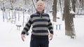 An elderly European man does a morning outdoor warm-up in the winter, exercise for a warm-up of the back, leanings